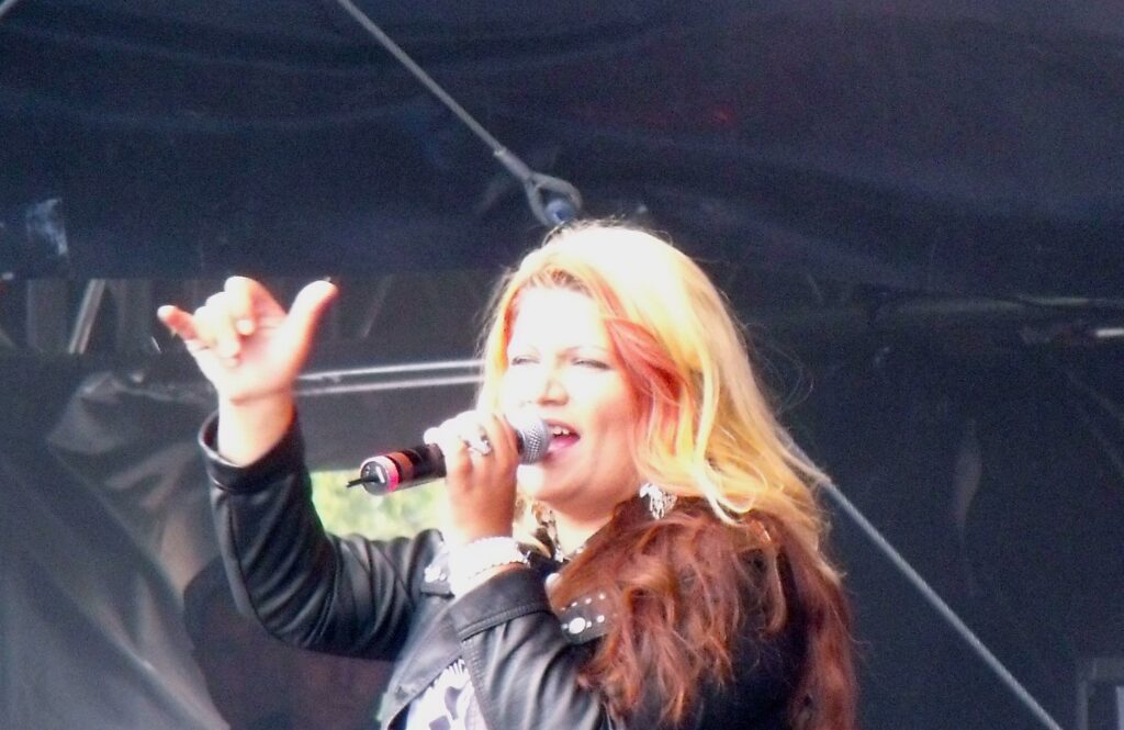 File:Mell Groove Coverage.JPG - a woman singing into a microphone on stage