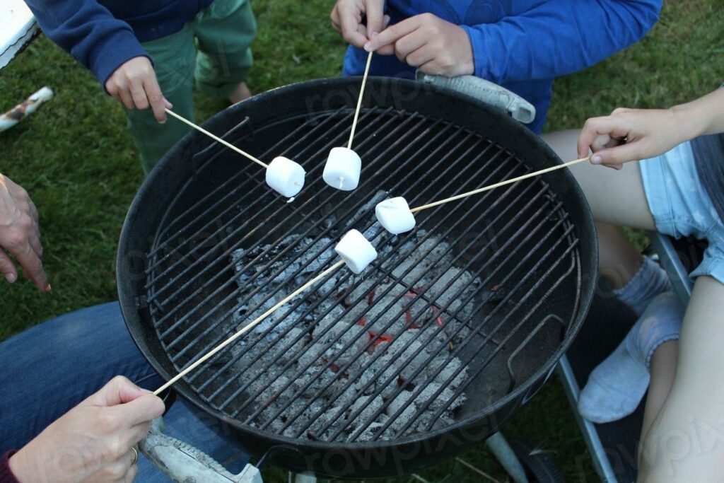 Grilling marshmallows over charcoal - a group of people sitting around a grill