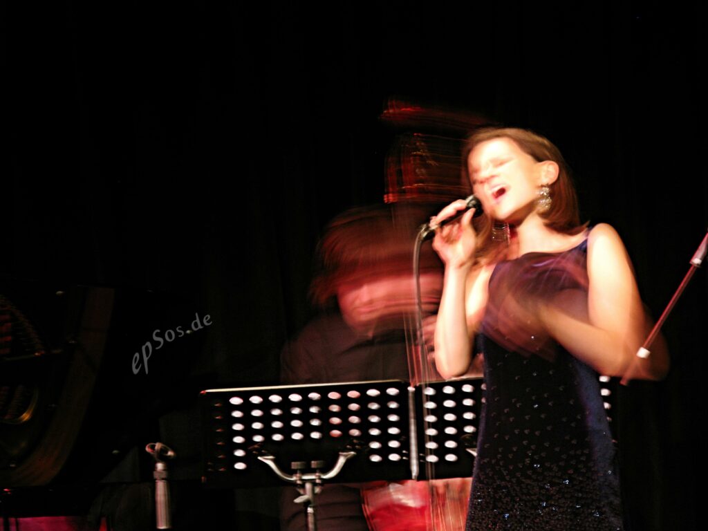 Artist Woman Singing Concert in Jazz Club - a woman singing into a microphone while a man plays the