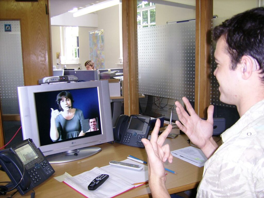 Deaf or HoH person at his workplace using a Video Relay Service to communicate with a hearing person