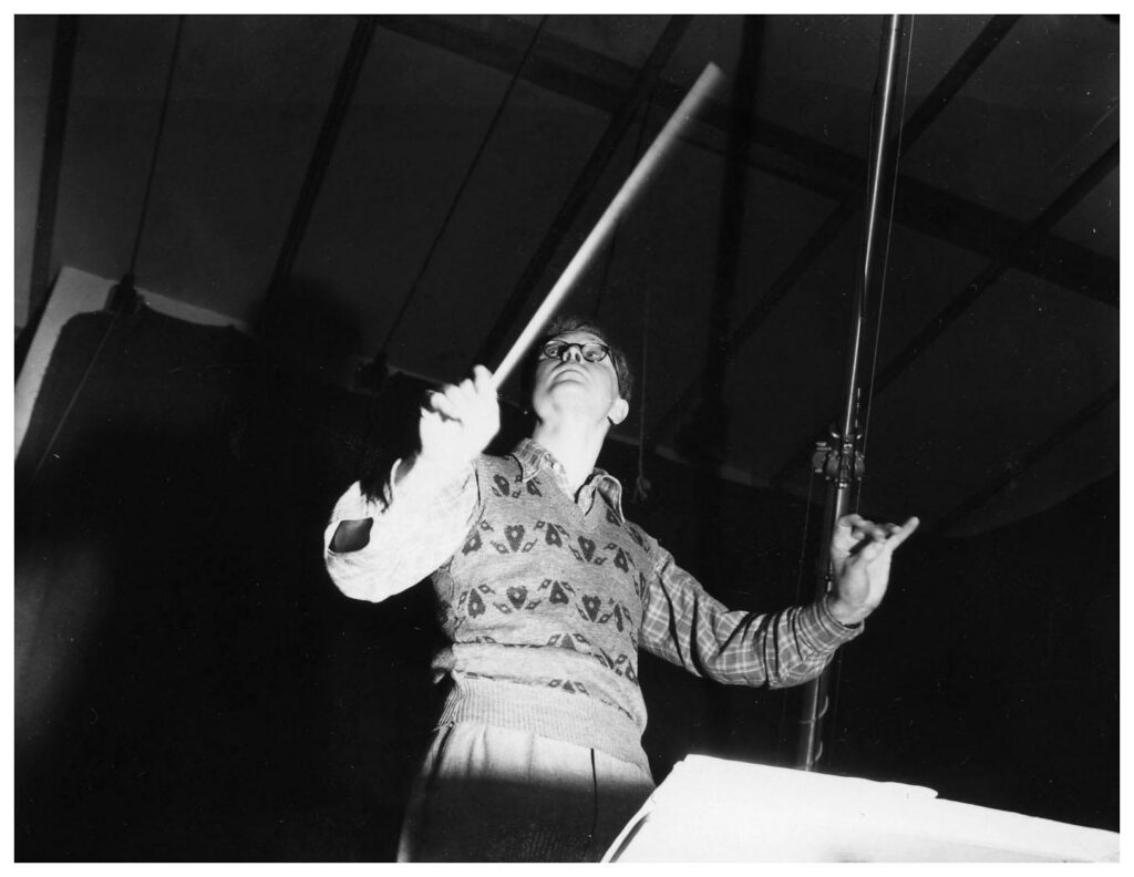 File:Douglas Lilburn (26217792433).jpg - a man in a hat and shirt holding a microphone