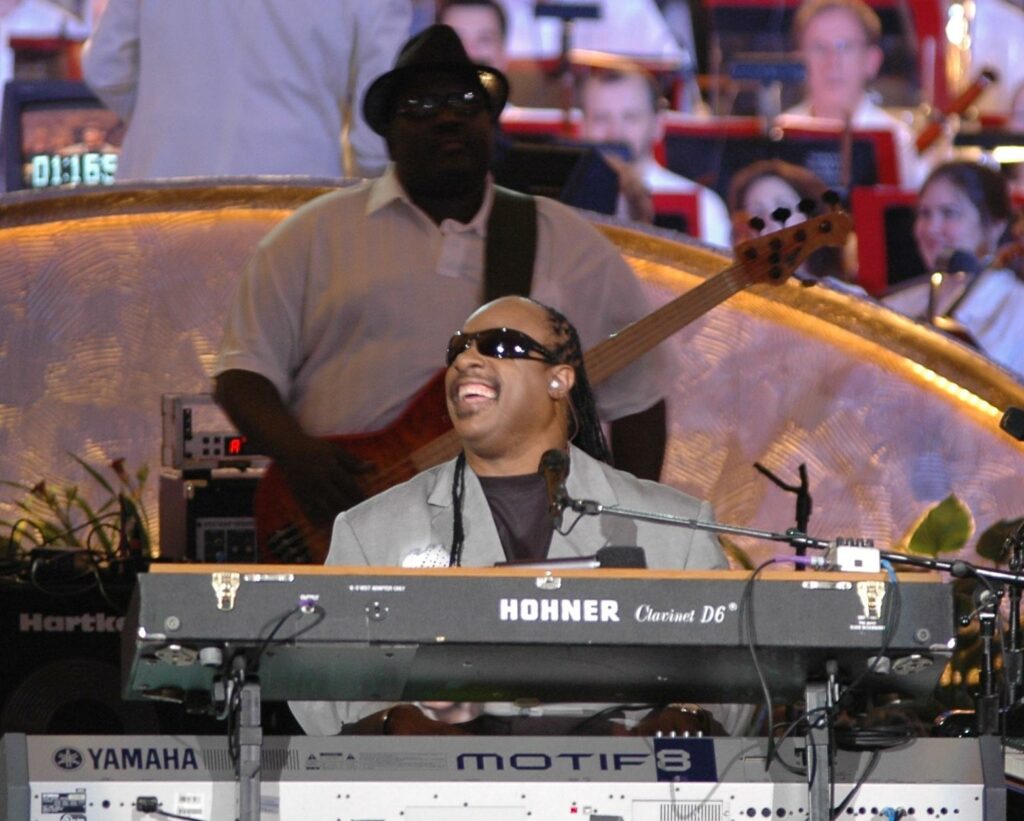 File:Stevie Wonder and Nathan Watts (2006).jpg - a man in a suit and sunglasses playing a keyboard