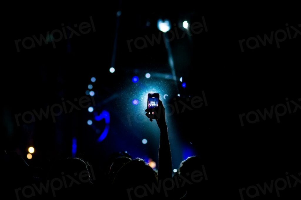 The silhouette of a person - a person holding a cell up to a crowd